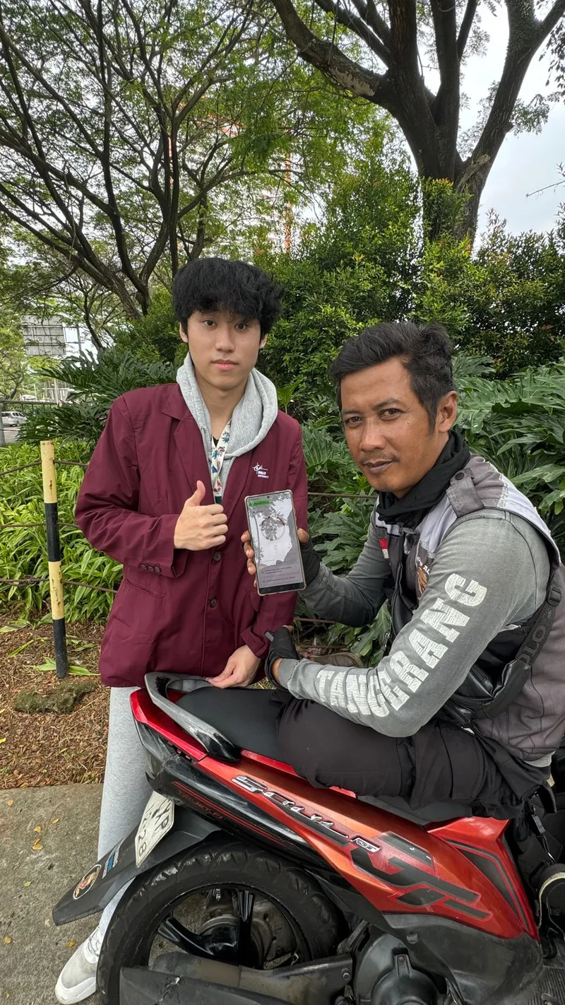 A student standing with an online driver on his motorbike, presenting the app on a phone