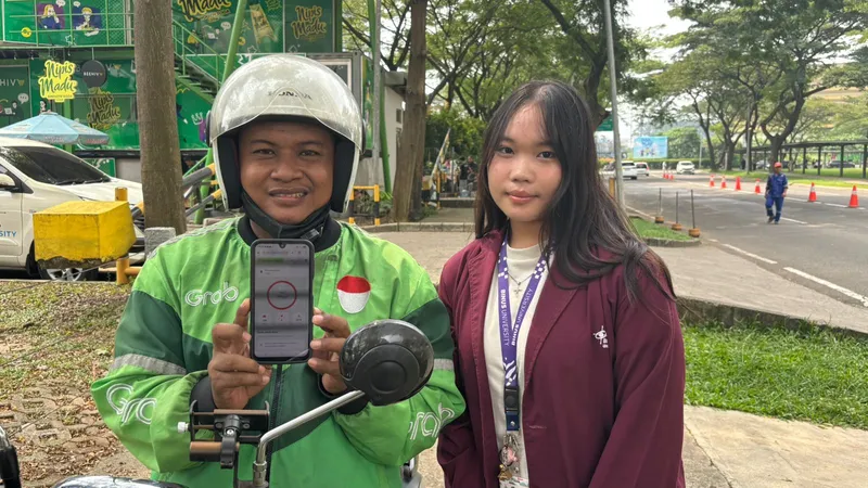 A helmeted online driver showing the app on his phone beside a student at the roadside