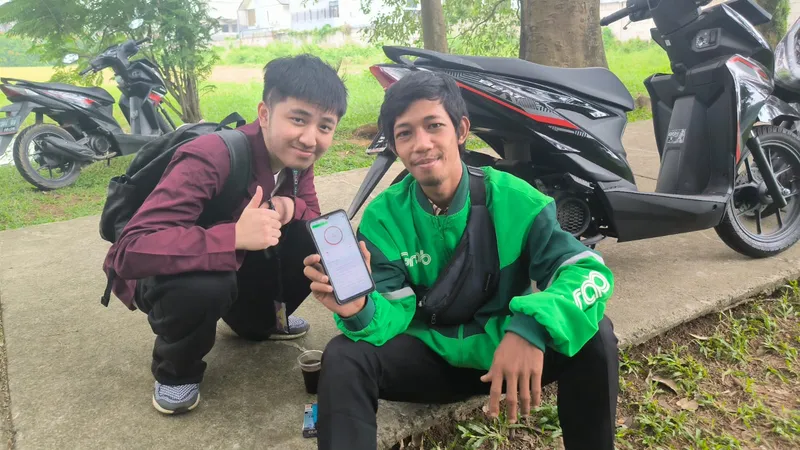 A student and an online driver crouching next to motorbikes, holding a phone that shows the app