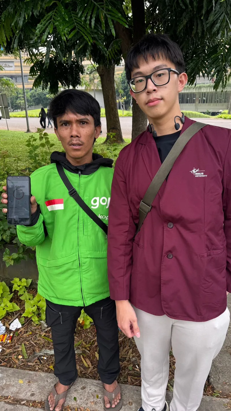 An online driver in a green jacket holding up a phone with the app, next to a student